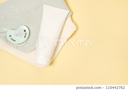 white cream tube and baby pacifier on yellow table background. Care about clean and soft body skin. Daily children beauty product white cream tube and baby pacifier on yellow table background. Care about clean and soft body skin. Daily children beauty product 110442762