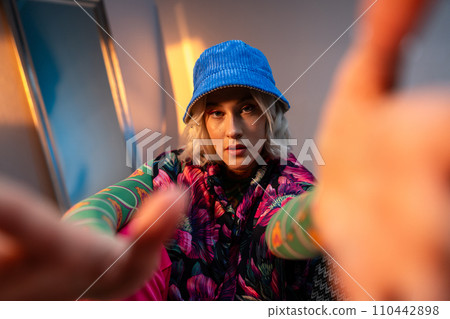 Cool hipster girl looking at camera. Wearing stylish outfit looking at camera and correcting her hat 110442898