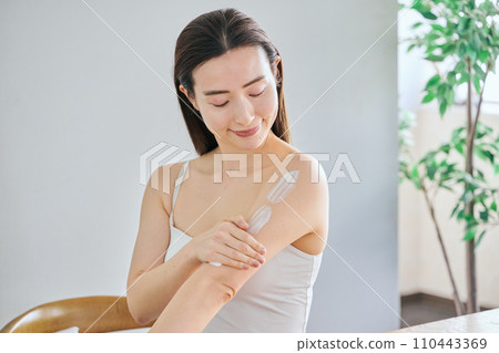 A woman in her 30s applying cream to her upper arms to take care of her body 110443369