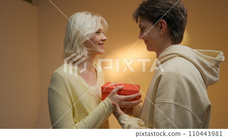 Happy man giving gift to his girlfriend on beige studio background, free space. Happy man giving gift to his girlfriend on beige studio background, free space. 110443981