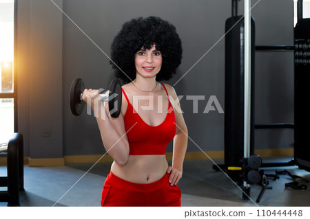 Girl with heavy dumbbells working out biceps on her arms 110444448