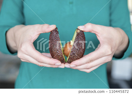 Hand holding fresh avocado close-up. The process of opening an avocado to replace butter on sandwiches. Hand holding fresh avocado close-up. The process of opening an avocado to replace butter on sandwiches. 110445872