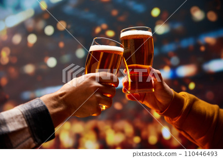 Two hands clinking with mug of cold foamy beer. People celebrating start of Oktoberfest. Selective focus. Blurred. Two hands clinking with mug of cold foamy beer. People celebrating start of Oktoberfest. Selective focus. Blurred. 110446493