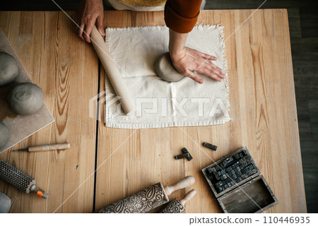 Female potter preparing clay for modelling on a table, top view. Potter kneading and rolling clay, preparing for hand modelling Female potter preparing clay for modelling on a table, top view. Potter kneading and rolling clay, preparing for hand modelling 110446935
