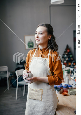 Portrait of a beautiful smiling pottery workshop leader. A middle-aged female potter with clay in her hands Portrait of a beautiful smiling pottery workshop leader. A middle-aged female potter with clay in her hands 110446936
