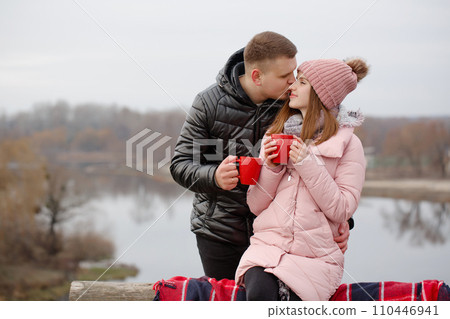 Young couple drinking a hot drink outside by the river 110446941