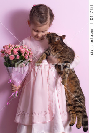 A cute little girl and a cat in a pink dress holds a bouquet of pink roses A cute little girl and a cat in a pink dress holds a bouquet of pink roses 110447131