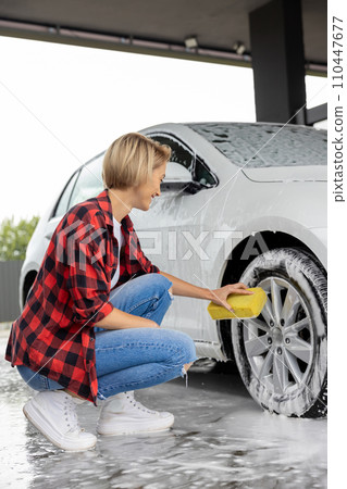 Blonde woman in checkered shirt washing a white car Blonde woman in checkered shirt washing a white car 110447677