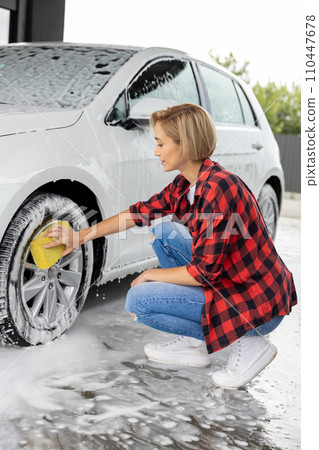 Blonde woman in checkered shirt washing a white car 110447678