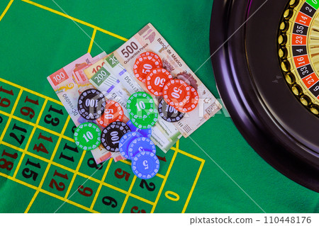 An casino roulette table with Mexican peso banknotes, poker chips is displayed on green gaming surface 110448176