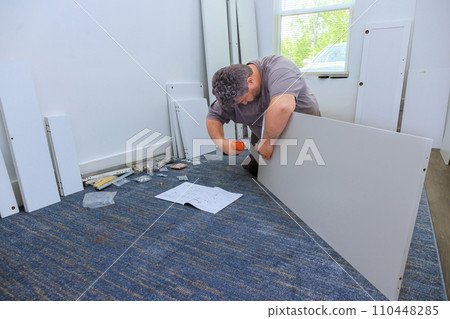 Using screwdriver, carpenter assembles closet cabinet for furniture Using screwdriver, carpenter assembles closet cabinet for furniture 110448285