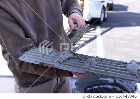 Tiler spreads wet cement adhesive with trowel before laying ceramic tiles Tiler spreads wet cement adhesive with trowel before laying ceramic tiles 110448340