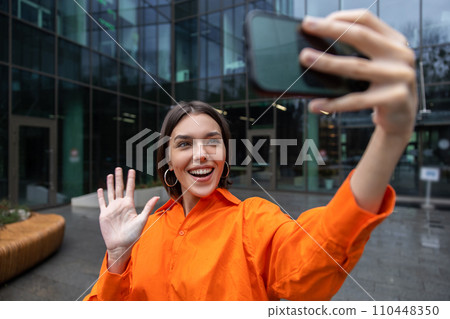 Girl in orange making selfie and smiling Girl in orange making selfie and smiling 110448350