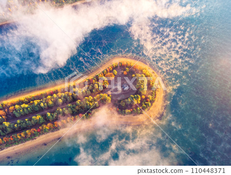 During autumn, misty fog blankets landscape over pond in early hours of morning 110448371