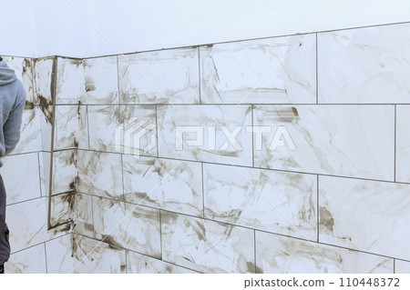 Ceramic tiles are grouted with rubber trowel by tilers filling gap between tiles. 110448372