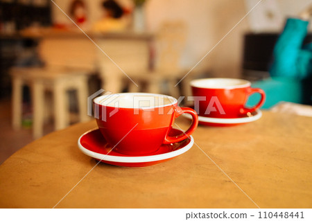 Close-up of two red cups of coffee on wooden rustic background with beautiful latte art. Delicious breakfast. 110448441