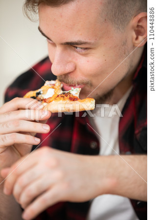 A young man eating a slice of pizza with cheese and tomato sauce. A young man eating a slice of pizza with cheese and tomato sauce. 110448886