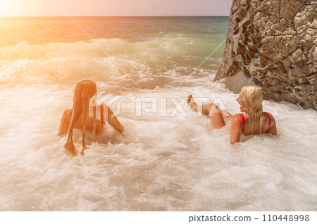 Women ocean play. Seaside, beach daytime, enjoying beach fun. Two women in red swimsuits enjoying themselves in the ocean waves. 110448998