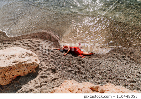 Woman red dress sea. Female dancer in a long red dress posing on a beach with rocks on sunny day 110449053