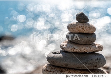 Tower of stones. Balanced pebble pyramid on the beach on a sunny day. Blue sea on the background. Selective focus, bokeh. Zen stones on the sea beach, meditation, spa, harmony, tranquility, balance 110449120