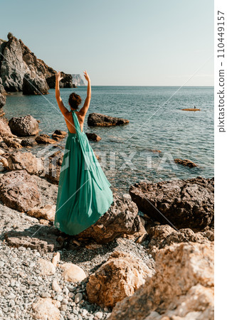 Woman green dress sea. Woman in a long mint dress posing on a beach with rocks on sunny day. Girl on the nature on blue sky background. Woman green dress sea. Woman in a long mint dress posing on a beach with rocks on sunny day. Girl on the nature on blue sky background. 110449157
