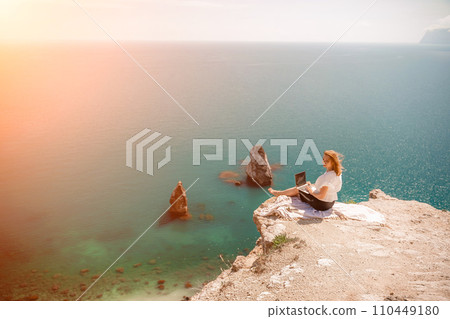 Freelance woman working on a laptop by the sea, typing away on the keyboard while enjoying the beautiful view, highlighting the idea of remote work. 110449180