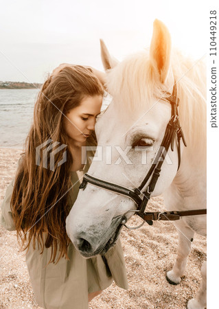 A white horse and a woman in a dress stand on a beach, with the A white horse and a woman in a dress stand on a beach, with the 110449218