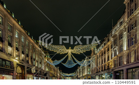Flying angel Christmas decoration led lights display. Dramatic view of the traditional Christmas decoration lights hanging above Regent Street during dusk. Flying angel Christmas decoration led lights display. Dramatic view of the traditional Christmas decoration lights hanging above Regent Street during dusk. 110449591