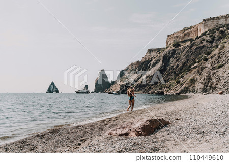 Woman beach vacation photo. A happy tourist in a blue bikini enjoying the scenic view of the sea and volcanic mountains while taking pictures to capture the memories of her travel adventure. 110449610
