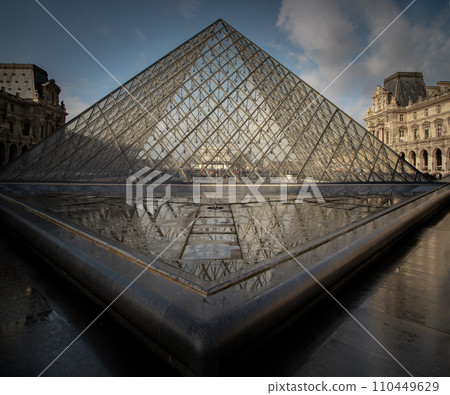 At the front of Famous Louvre Museum and its grand glass pyramid during day time with water reflection effect by after raining. 110449629