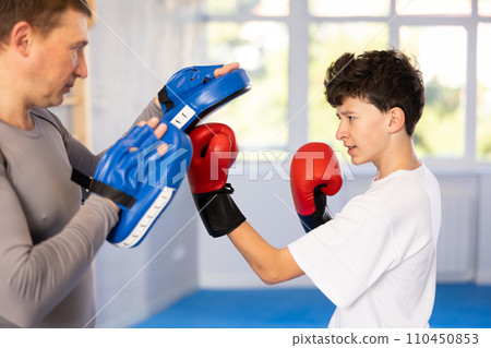 Teenage boy training boxing kicks on punch mitts held by instructor 110450853