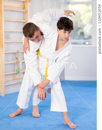 Teenage boy applying judo techniques on middle-aged trainer during sports classes Teenage boy applying judo techniques on middle-aged trainer during sports classes 110451034