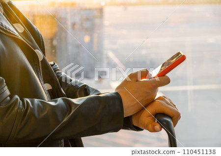 Woman in a black jacket checking her smartphone standing with a suitcase at the airport. Woman in a black jacket checking her smartphone standing with a suitcase at the airport. 110451138