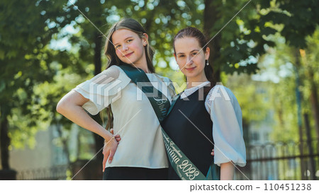 Two Russian schoolgirls graduate posing on a summer day. Two Russian schoolgirls graduate posing on a summer day. 110451238