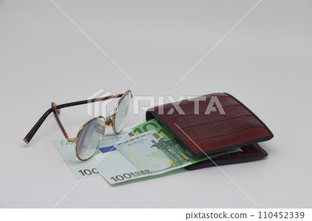 Brown wallet with banknotes and glasses. Brown frame. Symbol of accounting and family finance planning. Brown wallet with banknotes and glasses. Brown frame. Symbol of accounting and family finance planning. 110452339
