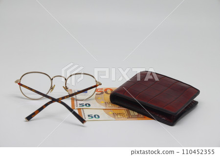 Brown wallet with banknotes and glasses. Brown frame. Symbol of accounting and family finance planning. Brown wallet with banknotes and glasses. Brown frame. Symbol of accounting and family finance planning. 110452355