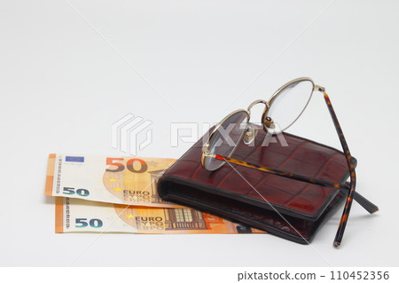 Brown wallet with banknotes and glasses. Brown frame. Symbol of accounting and family finance planning. Brown wallet with banknotes and glasses. Brown frame. Symbol of accounting and family finance planning. 110452356