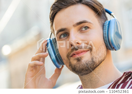 Happy bearded man in wireless headphones choosing, listening music dancing outdoors city street 110452361