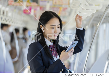 一名女高中生戴著耳機看著智慧型手機螢幕搭火車上學的圖片 一名女高中生戴著耳機看著智慧型手機螢幕搭火車上學的圖片 110452750