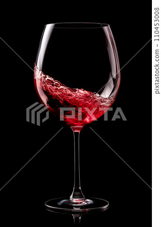 A glass with red wine is isolated on black background. Rose wine splashing in glassware. A glass with red wine is isolated on black background. Rose wine splashing in glassware. 110453008