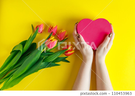 Female hands hold pink heart on yellow background. Tulips for valentine's day. Female hands hold pink heart on yellow background. Tulips for valentine's day. 110453963