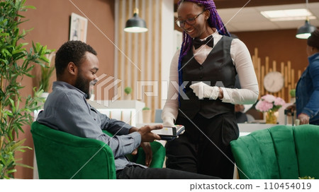 Man does mobile payment at pos, using nfc system to pay for cup of coffee in lounge area at five star hotel. Guest shows gratitude to staff member after providing excellent service. Handheld shot. 110454019