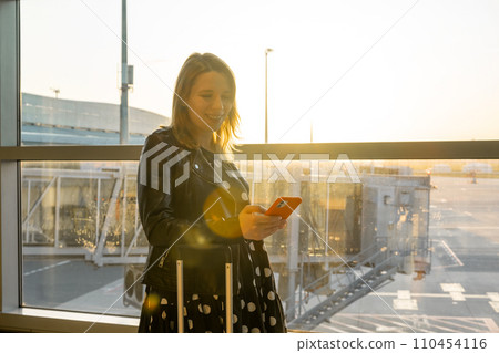 A young woman, checking her mobile phone, is prepared for boarding 110454116