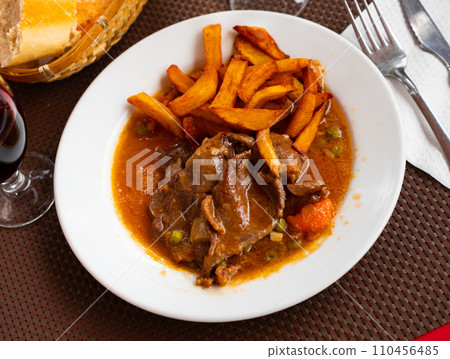 Veal stewed in gravy with side dish of fried potatoes 110456485