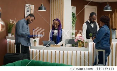 Travellers signing documents and finishing check in process at front desk reception, hotel concierge workers ensuring easy registration. Receptionist providing great service to guests on trip. 110456543