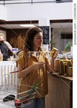 Green living woman in zero waste store interested in purchasing pesticides free produce with high nutritional value. Client does food shopping in environmentally friendly local neighborhood shop 110456639