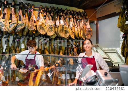 Young couple work together in butcher shop - they cut traditional Spanish jamon 110456681