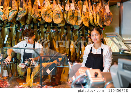 Positive young man and woman selling spanish jamon at counter 110456758