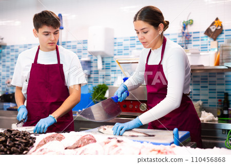 Female seller with knife cut fish in supermarket near counter Female seller with knife cut fish in supermarket near counter 110456868