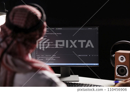 Muslim man sits at a computer and programs, exhibiting the app development process. Over-the-shoulder image of a computer monitor displaying code created by an Arab man dressed traditionally. Muslim man sits at a computer and programs, exhibiting the app development process. Over-the-shoulder image of a computer monitor displaying code created by an Arab man dressed traditionally. 110456906